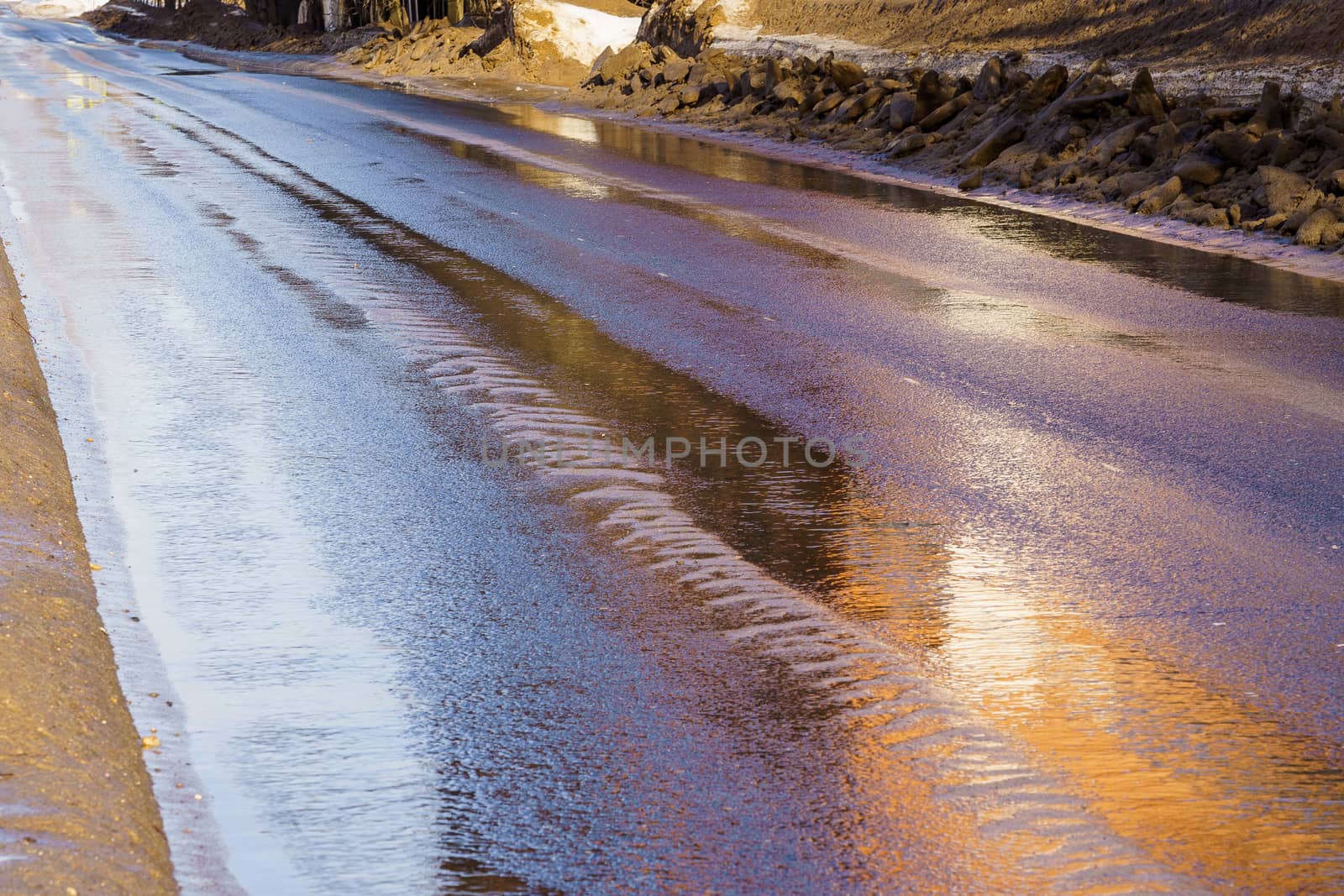 asphalt road in winter, with melting snow on the sides of the road and water
