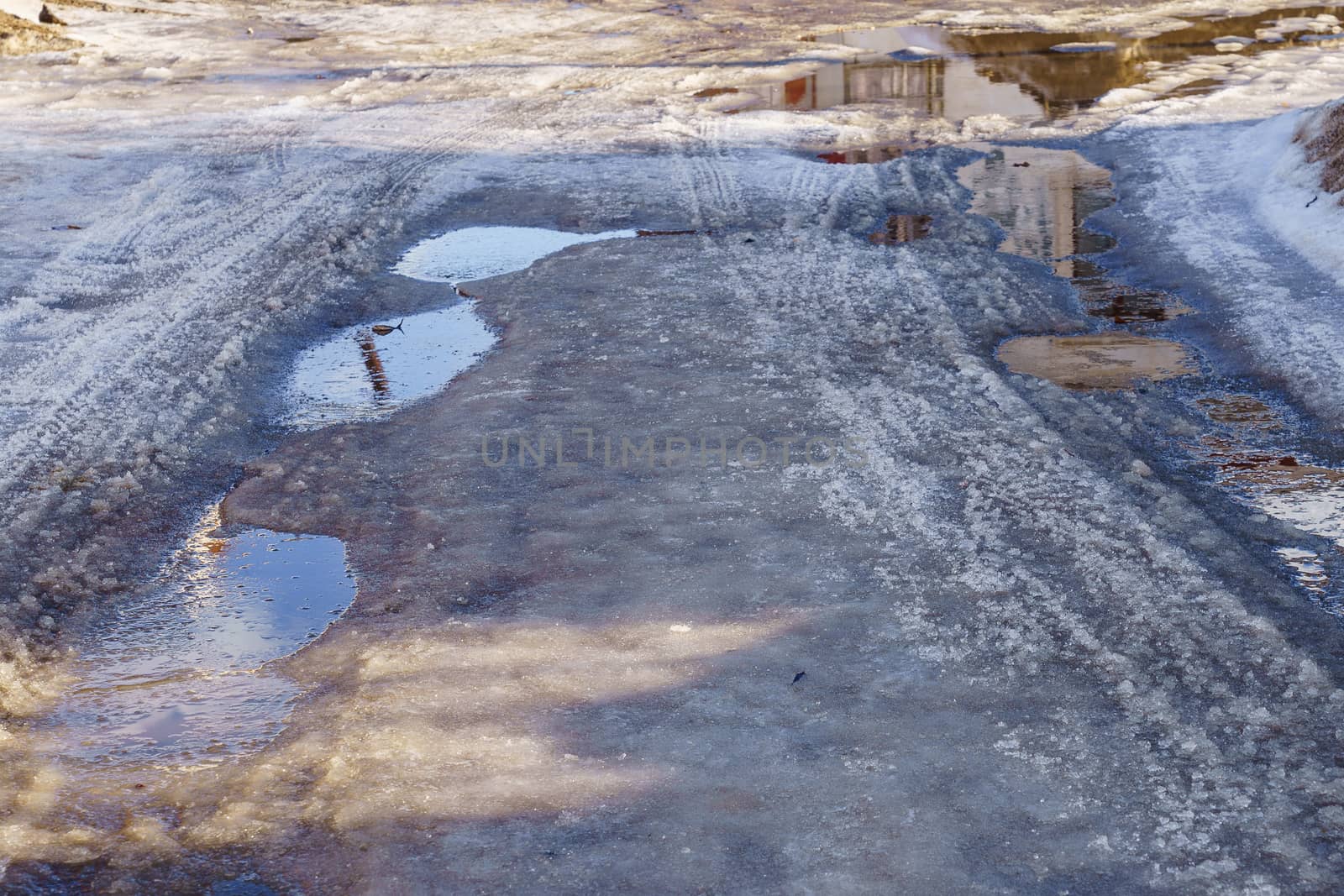 winter road covered with snow and ice with puddles and ruts, sunny day