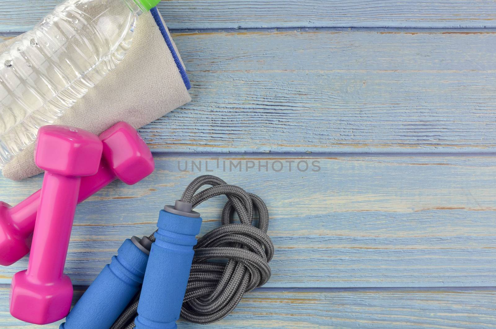 Top or flat lay view of dumbbells, towel, water and skipping rope with copy space area on blue wooden background. Healthy concept. Selective focus.