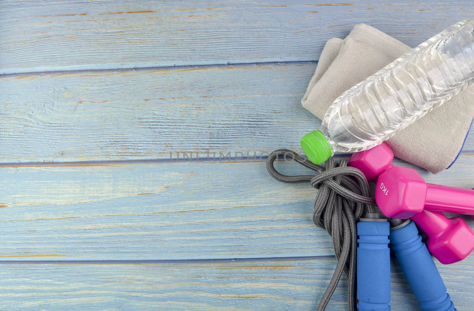 Top or flat lay view of dumbbells, towel, water and skipping rope with copy space area on blue wooden background. Healthy concept. Selective focus.