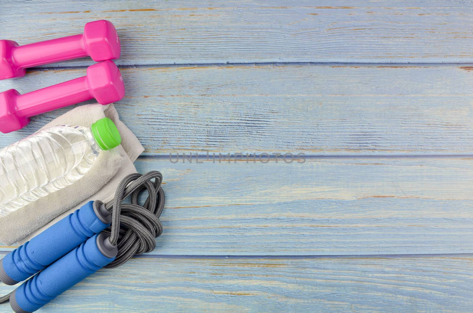 Top or flat lay view of dumbbells, towel, water and skipping rope with copy space area on blue wooden background. Healthy concept. Selective focus.