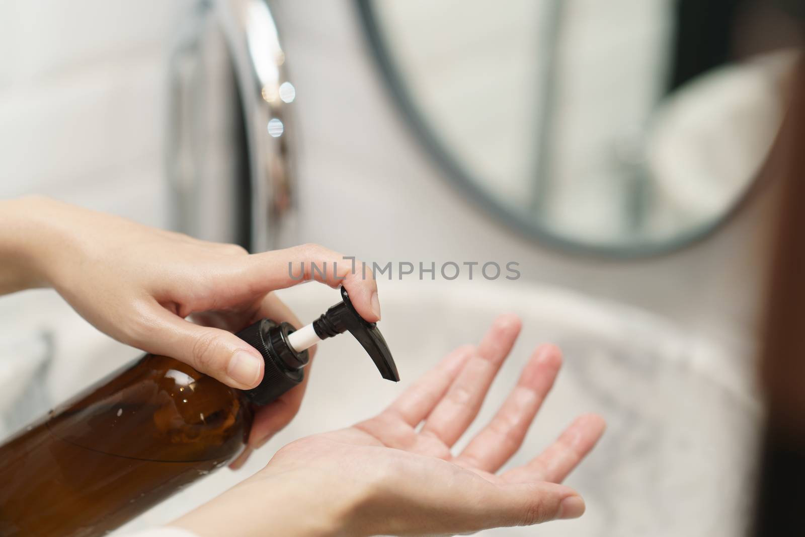 Woman washing hands with soap dispenser bottle at sink in bathroom.