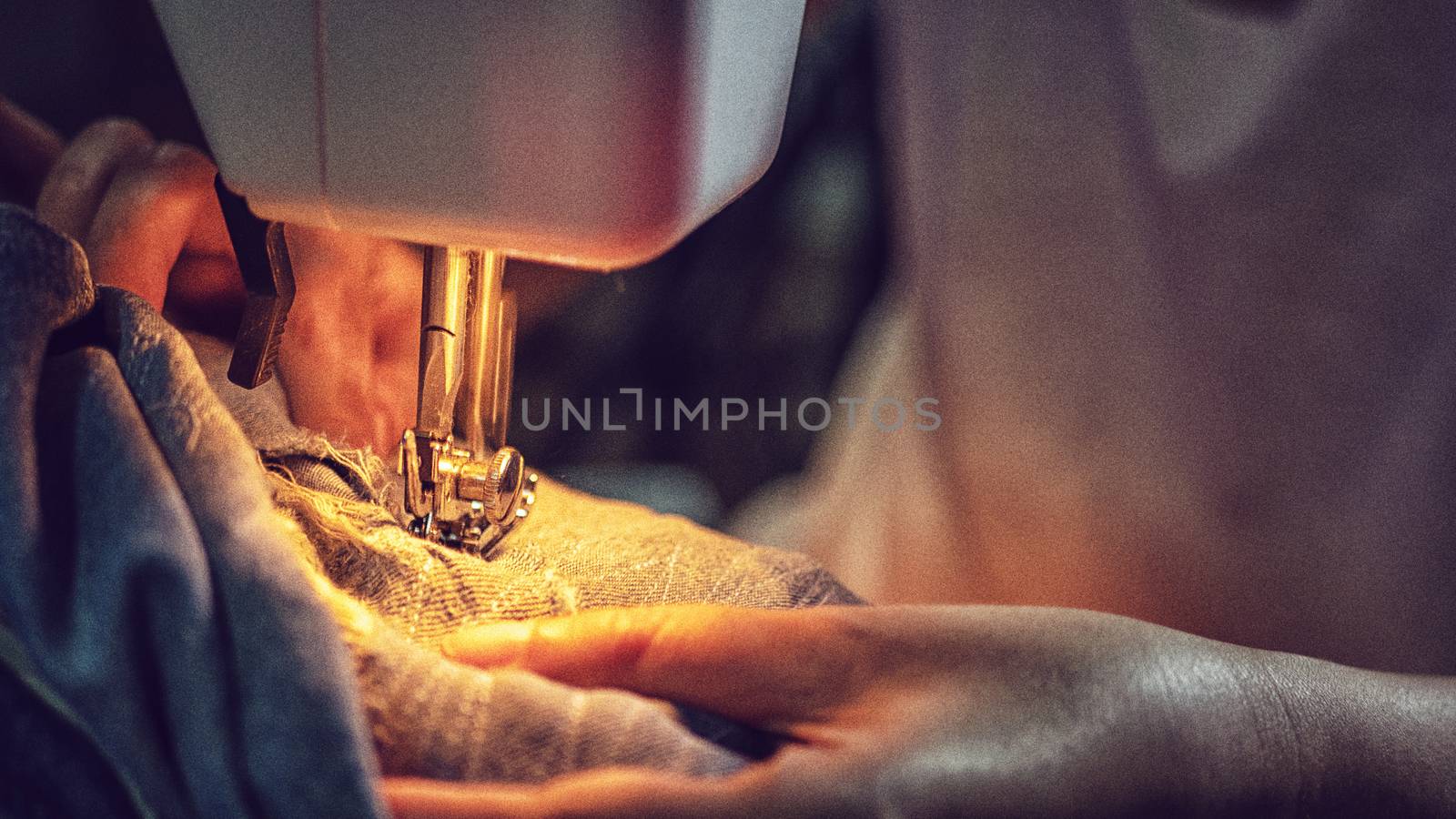 close up of a woman sewing blue denim jeans with a sewing machine by asiandelight