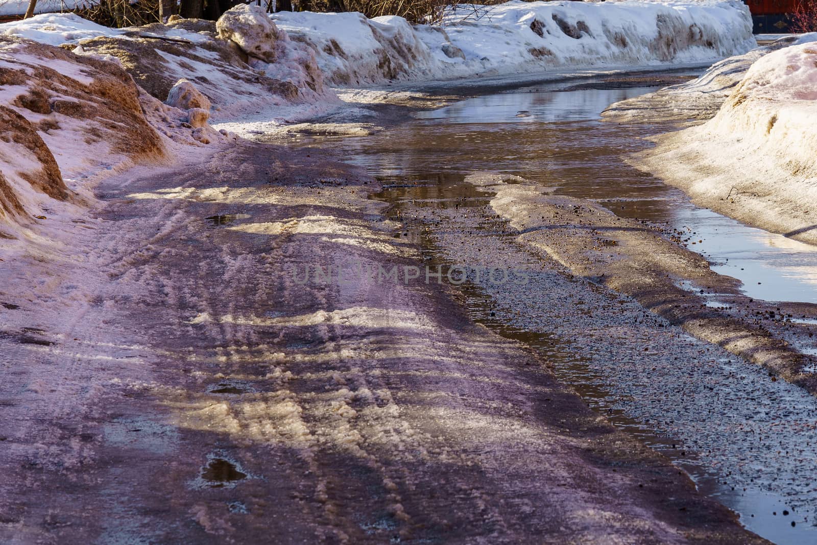winter road covered with snow and ice with puddles and ruts, sunny day