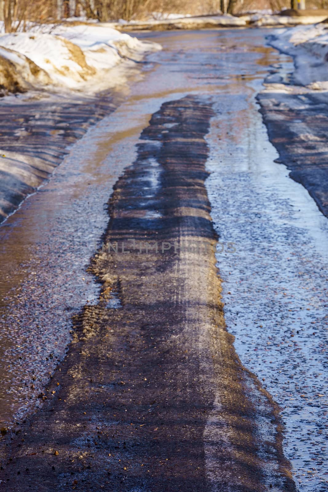 winter road covered with snow and ice with puddles and ruts by VADIM