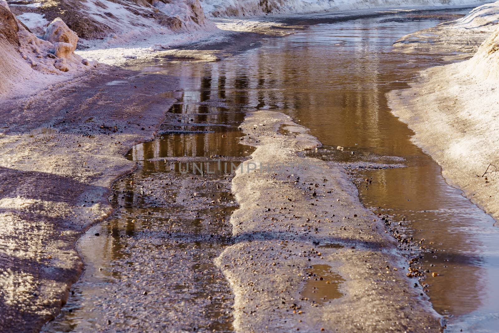 winter road covered with snow and ice with puddles and ruts, sunny day