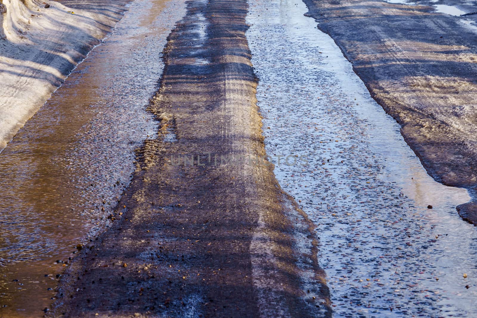 winter road covered with snow and ice with puddles and ruts, sunny day