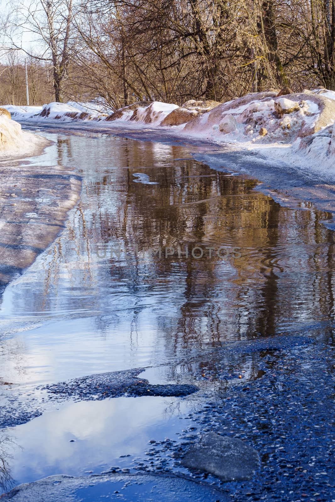 winter road covered with snow and ice with puddles and ruts, sunny day