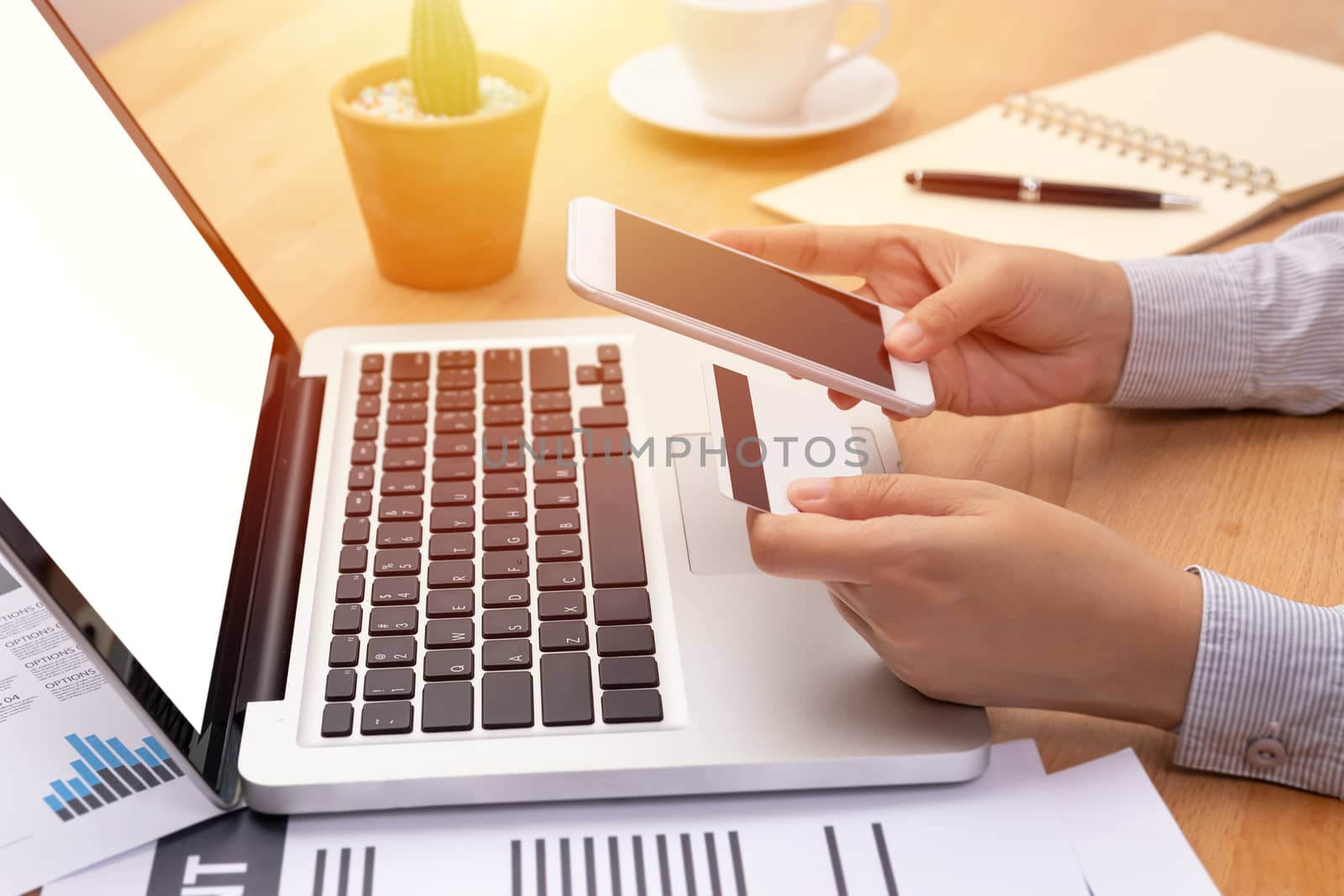 woman holding a credit card and purchase making online payment via mobile smartphone with blank screen in front of computer notebook laptop with blank screen in workplace