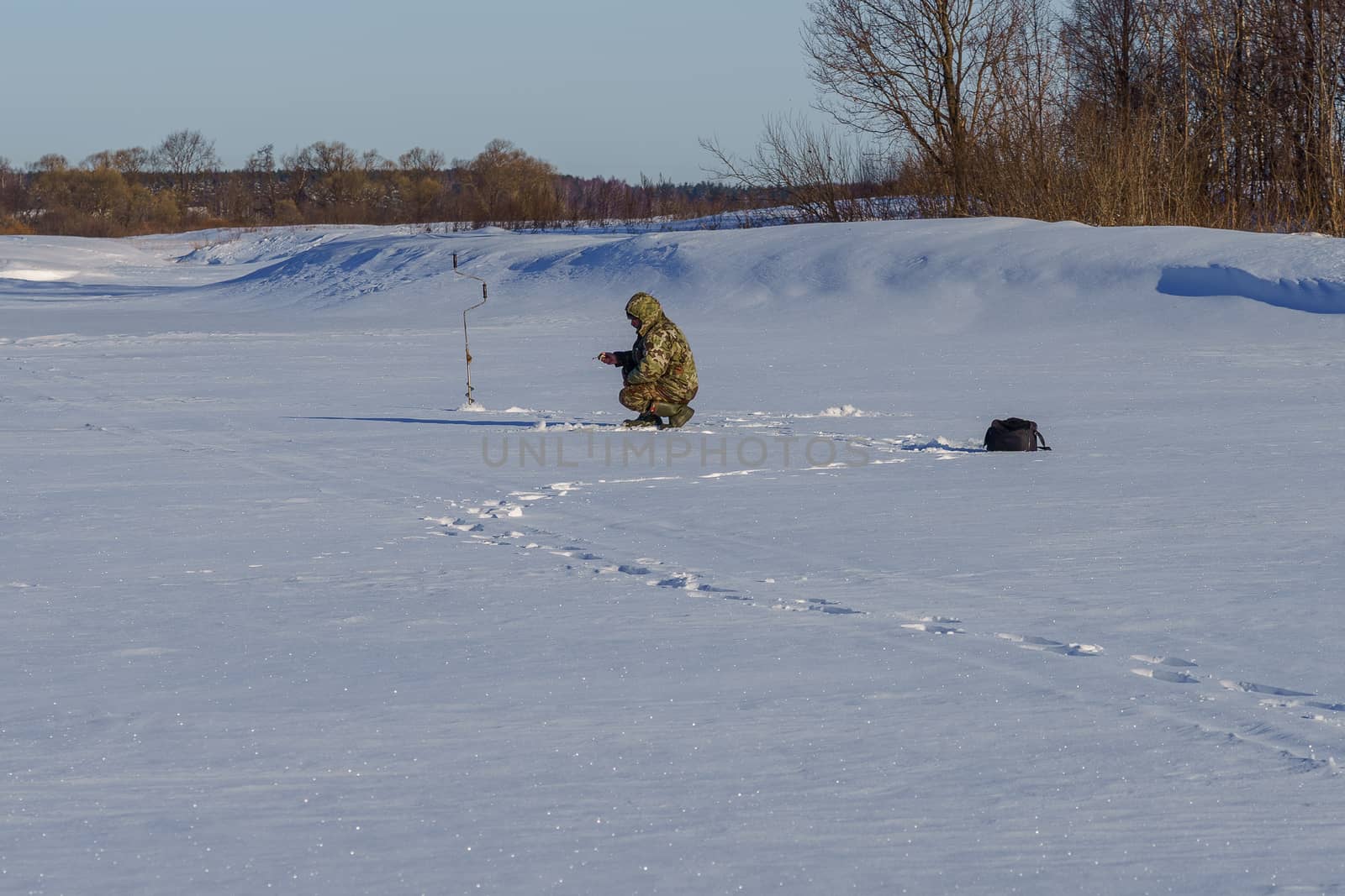 angler on ice with fishing rod on a sunny winter day