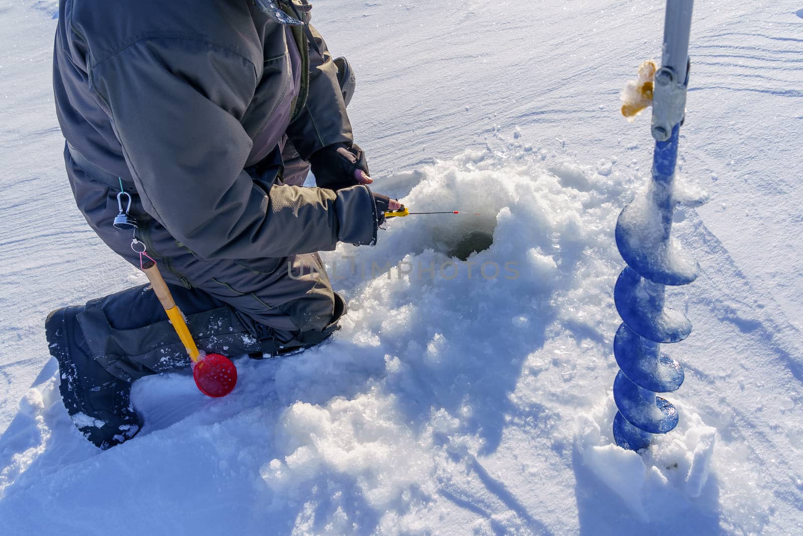 hands of a fisherman, a winter fishing pole and a drill in the ice, a plot on ice fishing