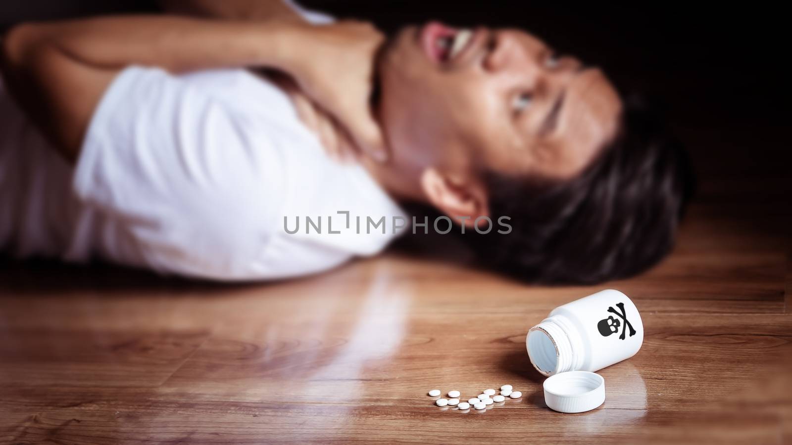 man lay on the floor of the room with symptoms of torture from eating poison for suicide, white bottle with the cross skull logo falls on the floor. problems of depression ,mental and stress patients by asiandelight