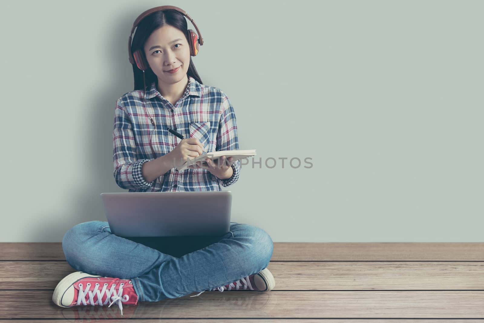 female student relaxed sitting on a wooden floor at home and watching training online course and listening it with headphones from compute laptop. online education service with modern study technology by asiandelight