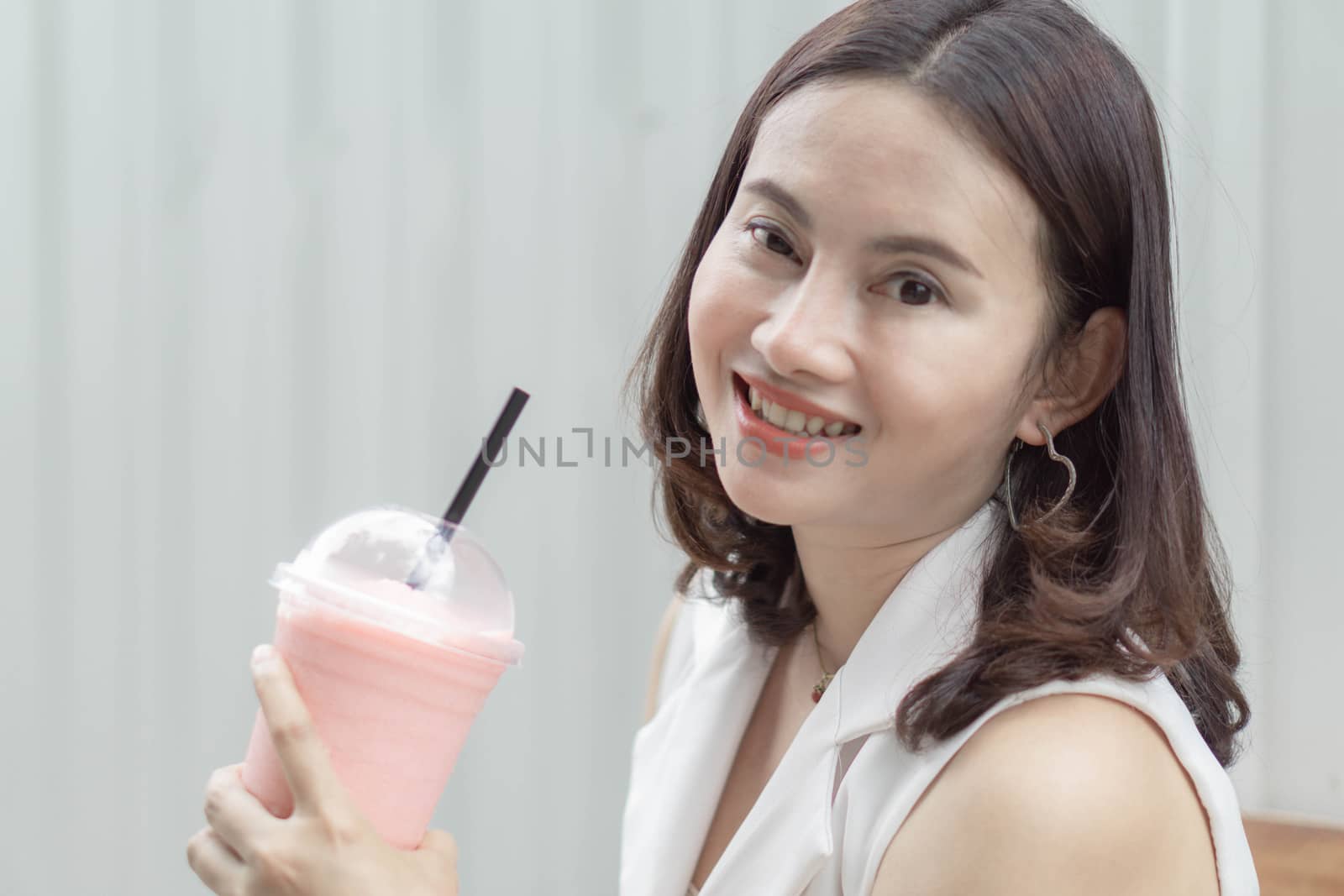 Closeup woman drinking strawberry smoothie and cake with green nature background, selective focus