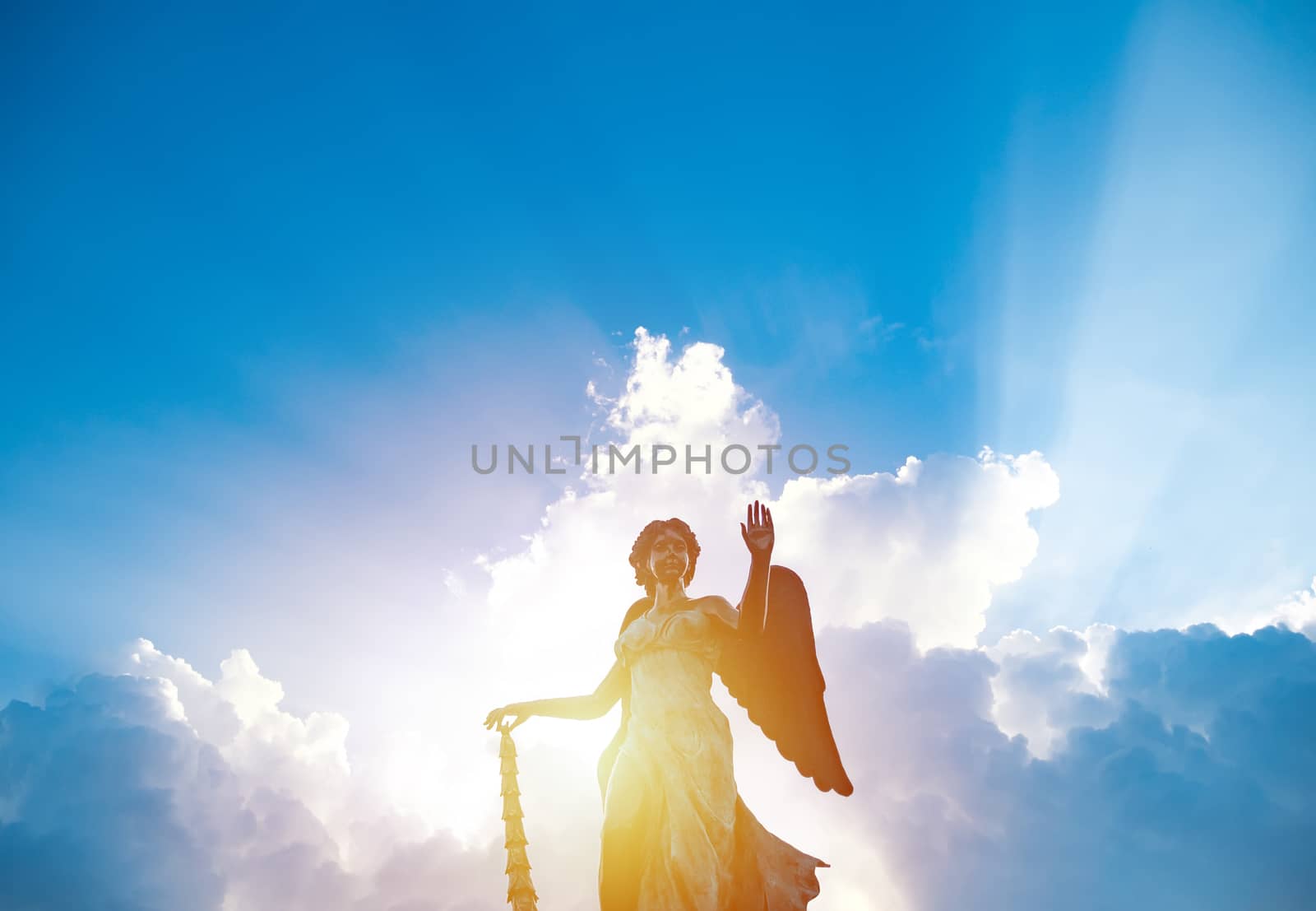 silhouette of angel statue sculpture with sunlight shining behind white cloud with blue sky background