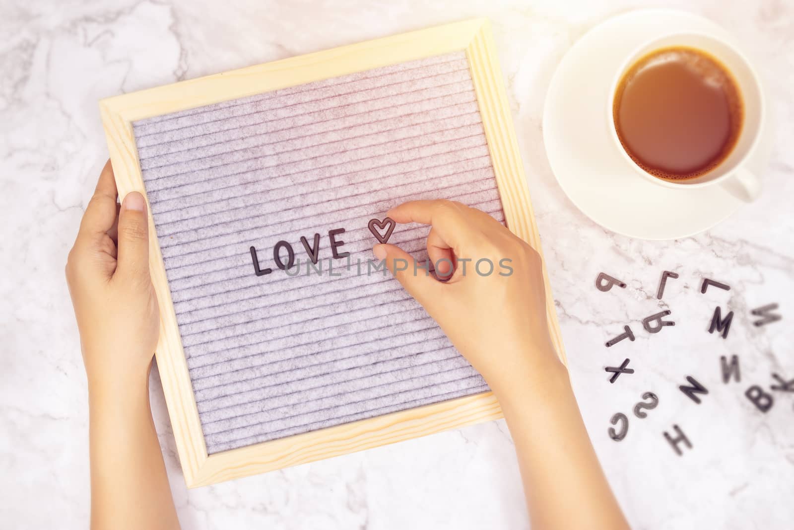 word LOVE on letter board with woman's hand holding heart symbol on white marble desk background with coffee cup