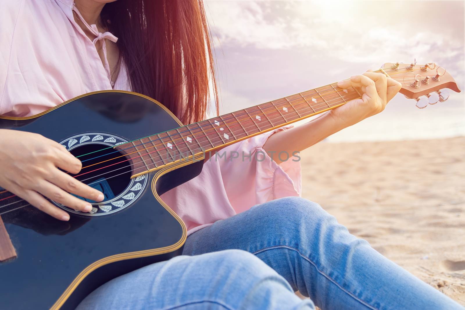 woman's hands playing acoustic guitar, capture chords by finger on sandy beach at sunset time. playing music concept by asiandelight