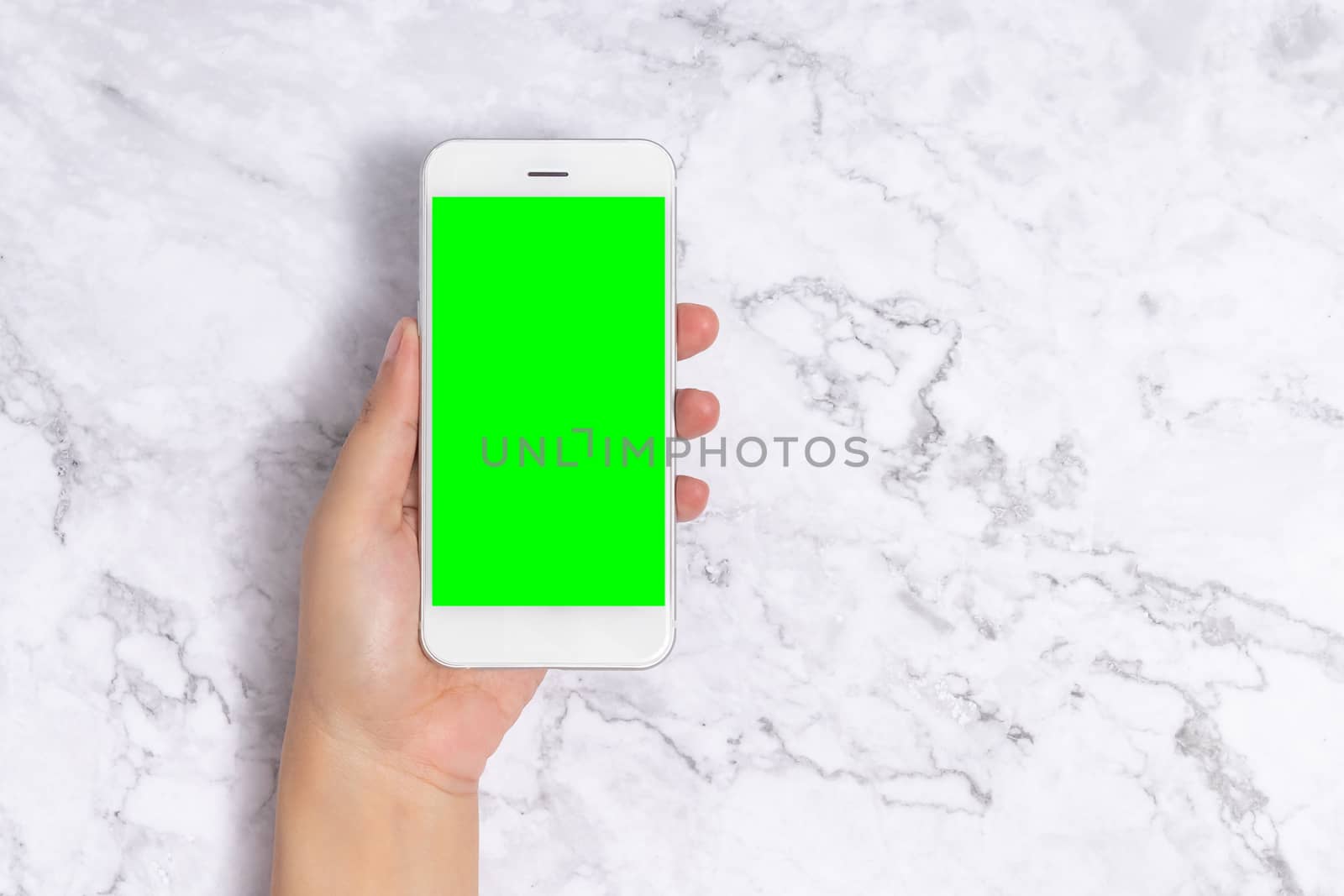close up woman hand holding white mobile phone with blank green screen on white marble background, front view with copy space. clipping path include by asiandelight
