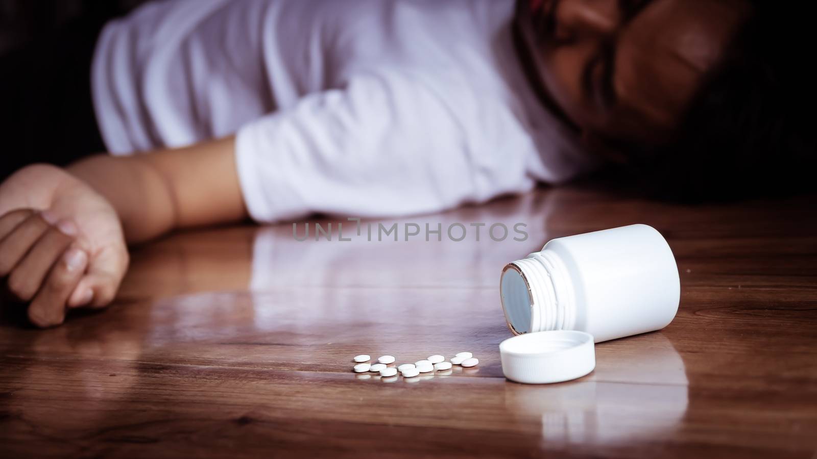 depression man committing suicide by overdosing on medication. close up of overdose pills from plastic medicine container with depress man on the floor
