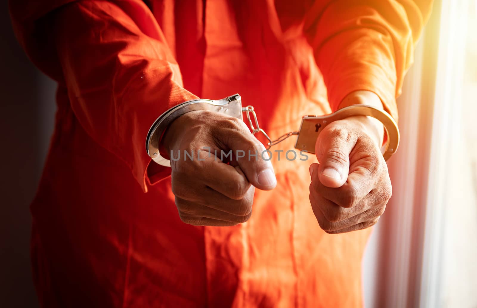close up of prisoner's hands with handcuffs in orange jumpsuit at prison by asiandelight