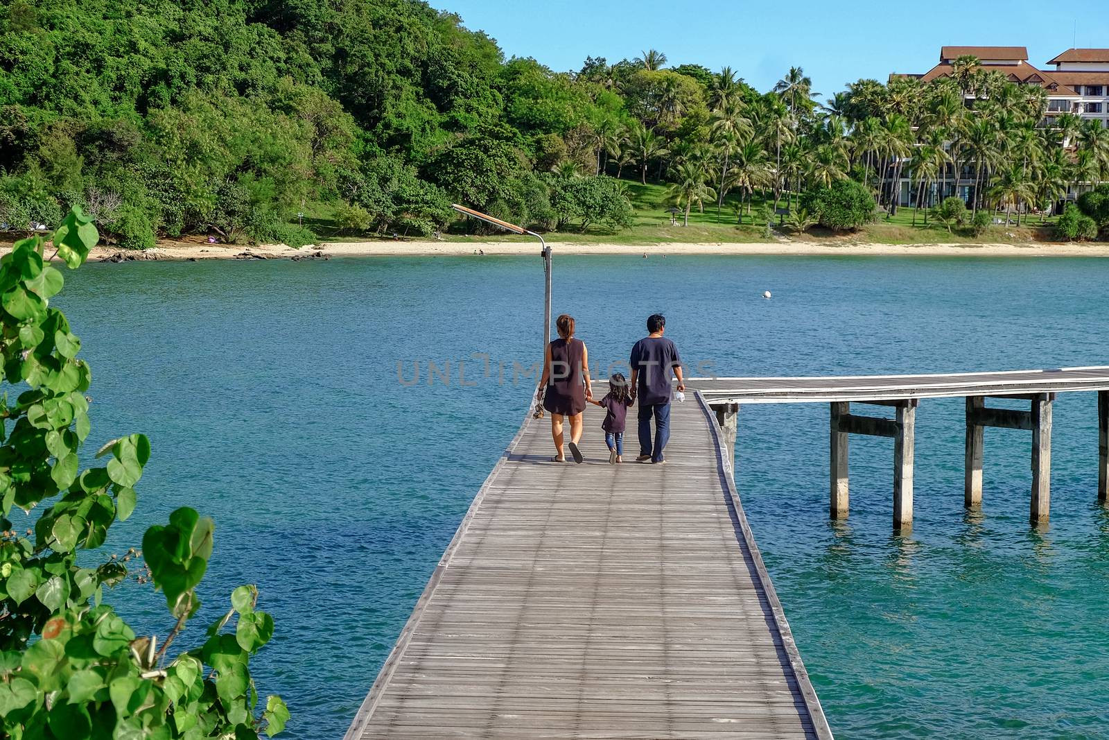 Family holiday with parents carrying children along the sea-side bridge at Khao Laem Ya National Park, Rayong, Thailand.