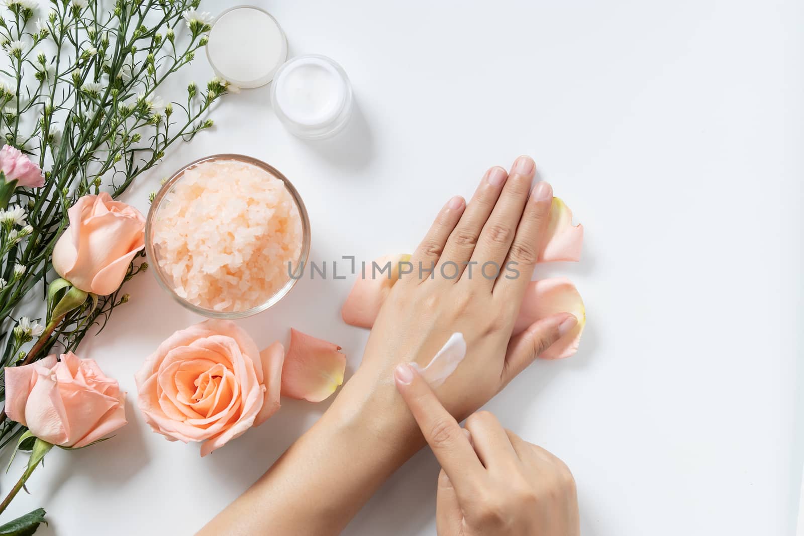 natural skincare concept. woman apply white cream on her hands on white background with jar of cosmetic cream, salt spa scrub ,rose and  white flowers with copy space