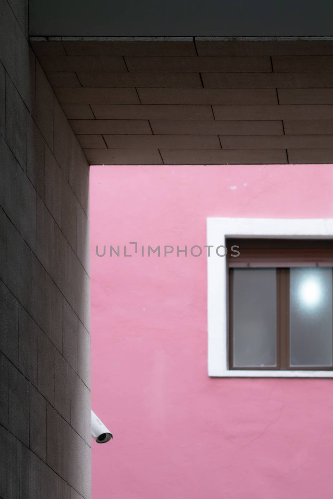 Composition of parallel and perpendicular lines with a window and a security camera on a magenta wall, framed with blocks of gray cement.