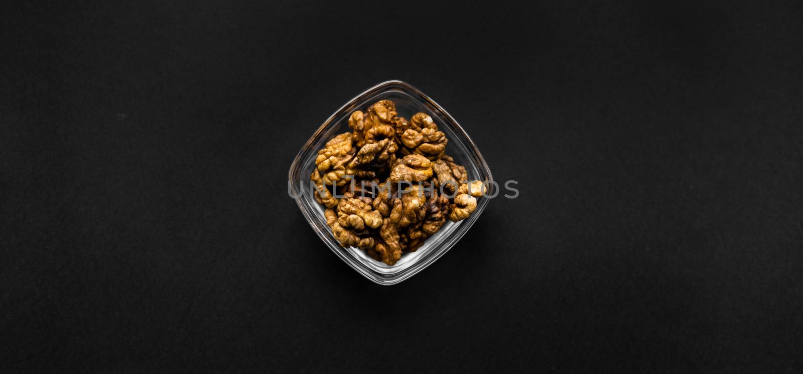 Walnut in a small plate on a black table. Walnuts is a healthy vegetarian protein nutritious food. Natural nuts snacks. by vovsht