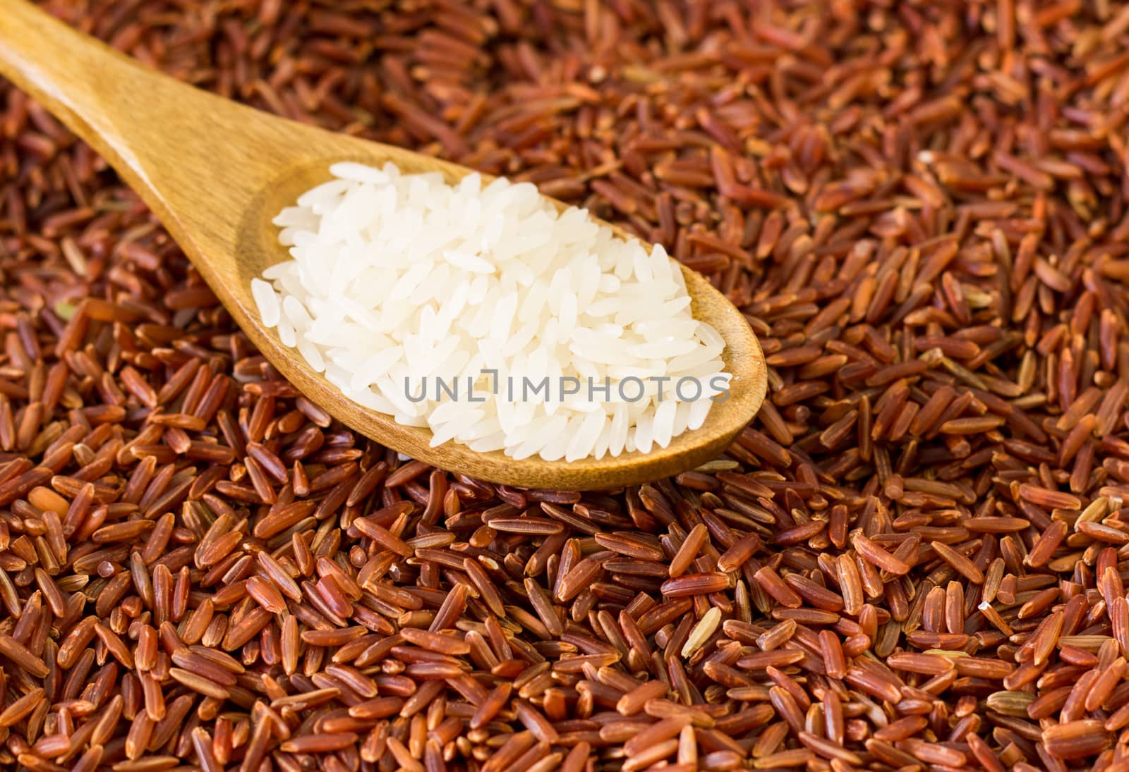White rice on wooden spoon on brown rice background