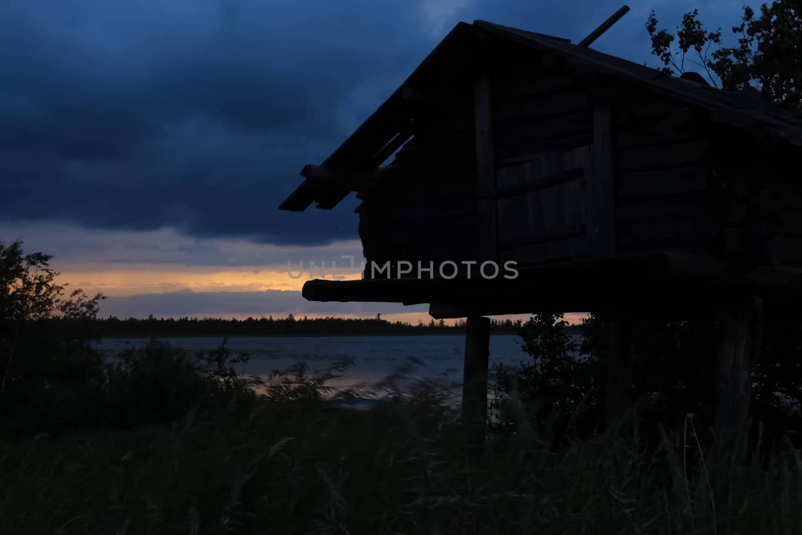 A house on stilts on the shore of the lake. Evening, twilight.
