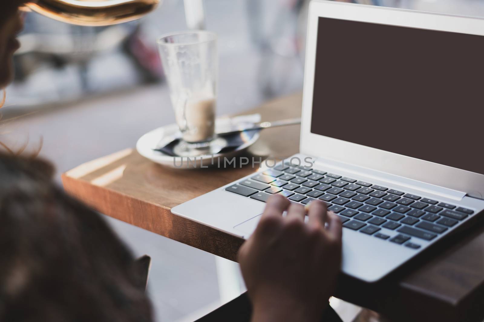 Mockup image of a woman using laptop with blank screen and drinking latte caffe in the restaurant.