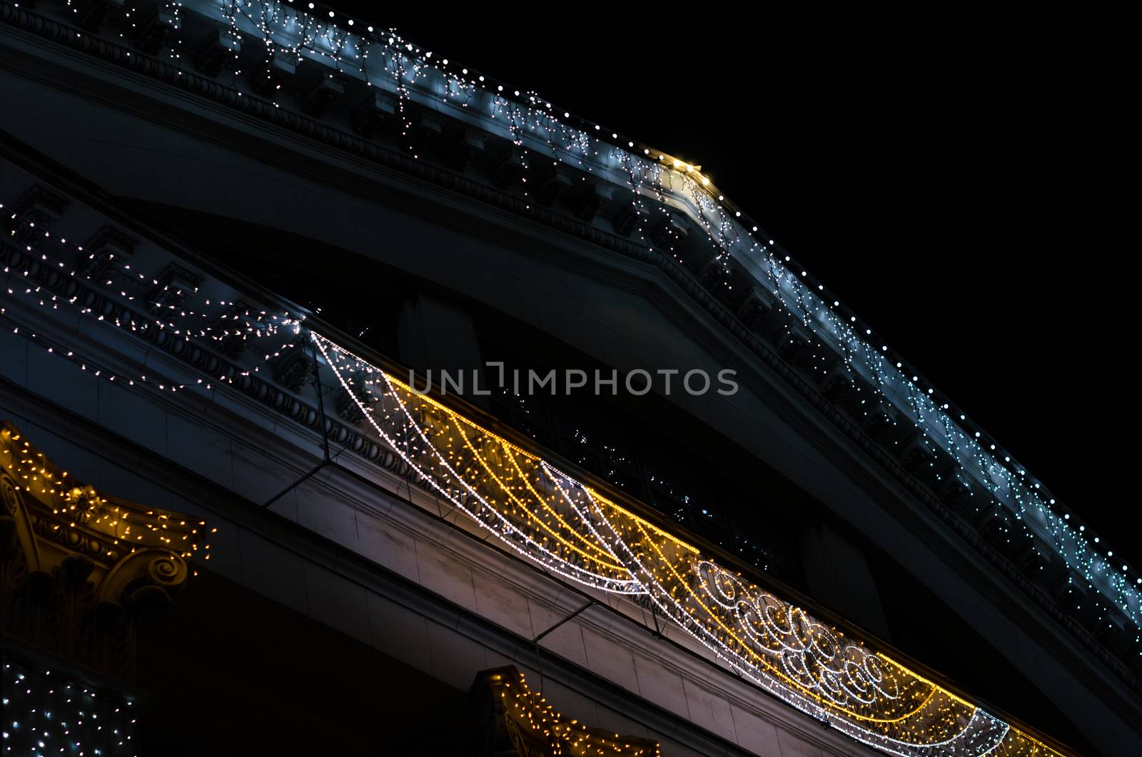 fragment of the facade and roof of a vintage building with colored lights decoration isolated on black background at night