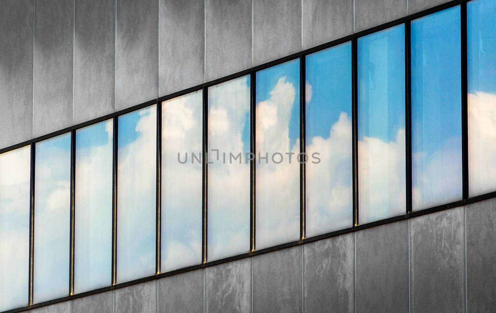 reflection of blue sky and white clouds in the windows of a gray building