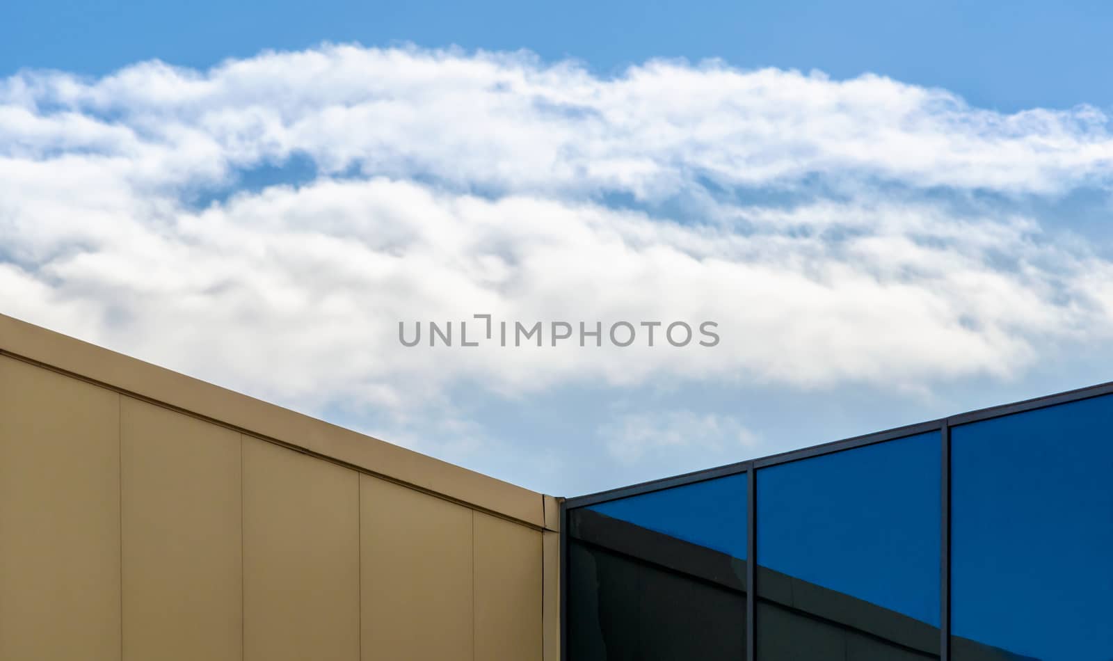 corner of a modern office building with a window and a blue sky with white clouds