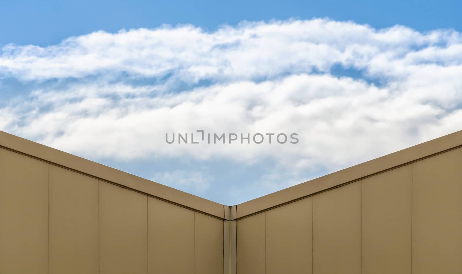 corner of a modern beige building and blue sky with white clouds