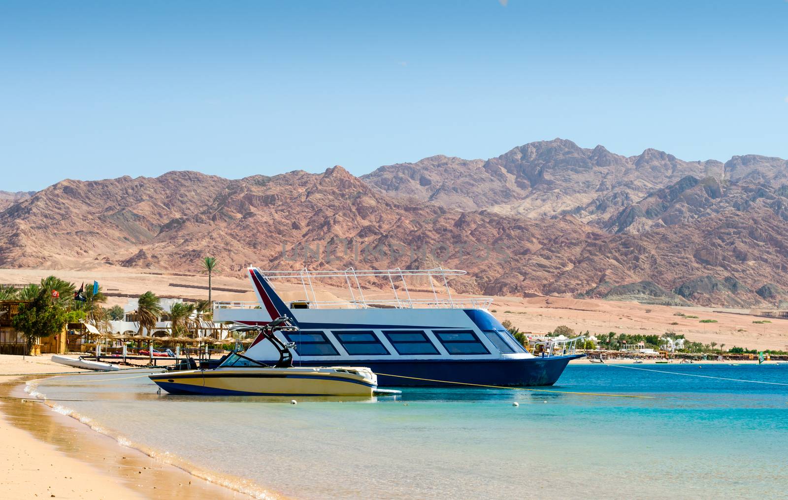 two boats at the surf on the background of the beach with palm trees and high rocky mountains in Egypt