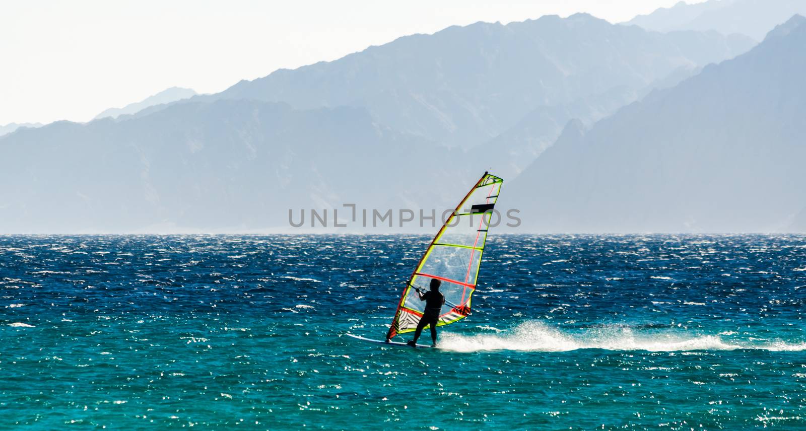 one surfer rides a sail in the Red Sea against the backdrop of the high mountains in Egypt