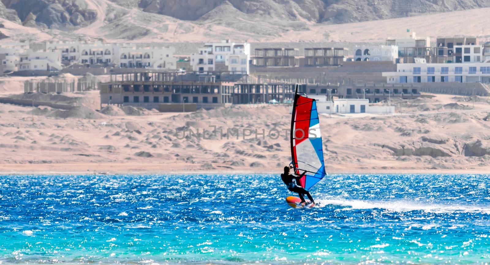 surfer with a colored sail rides in the Red Sea in Egypt against the backdrop of the beach and hotels