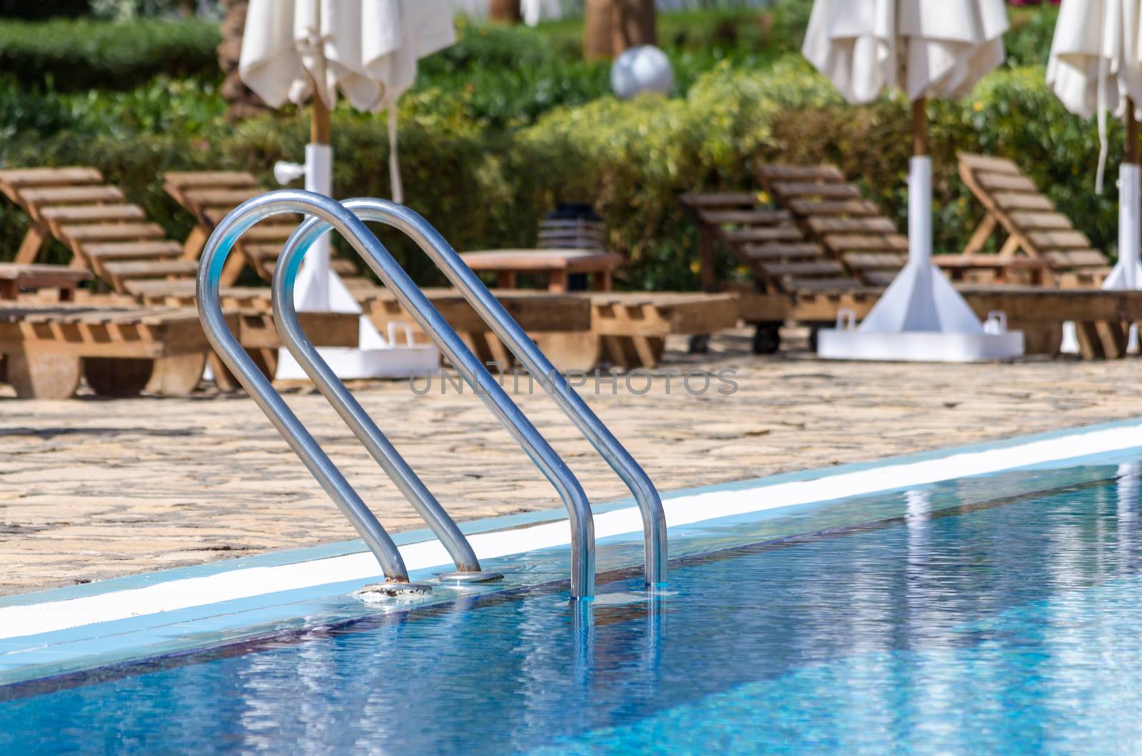 handrails by the pool with blue water on the background of sun loungers and folded white umbrellas