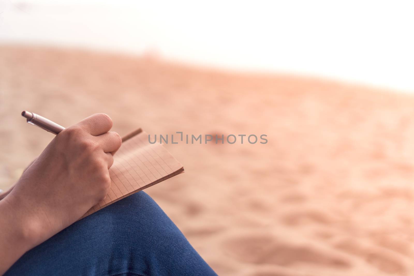 Woman hand writing down in small white memo notebook. by Suwant