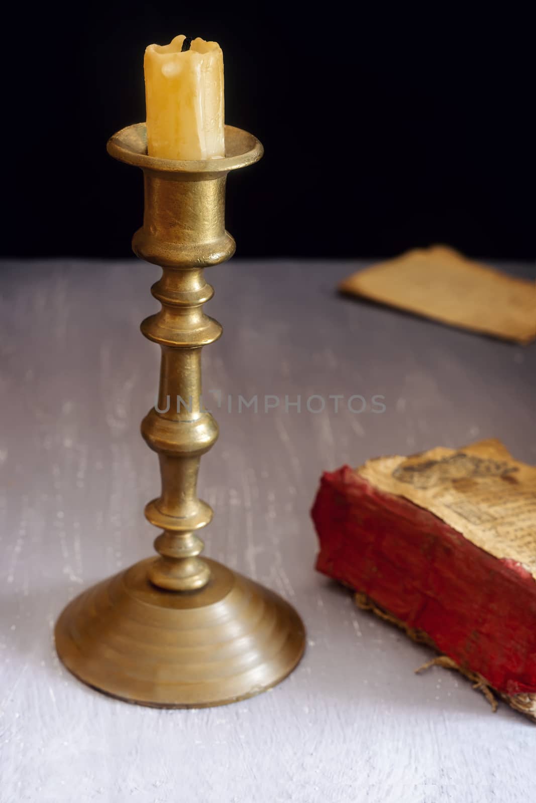 On the table, an old copper candlestick with a candle and an old book.