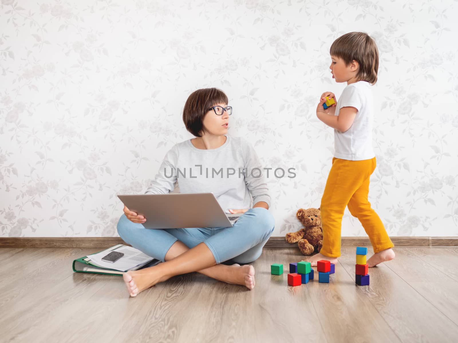 Mom and son at home. Mother works remotely with laptop, kid plays near her. Freelance work in same time with raising children.