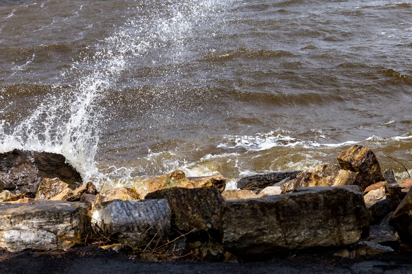 A splash of water flies into the air as waves hit rocks on a riverbank.