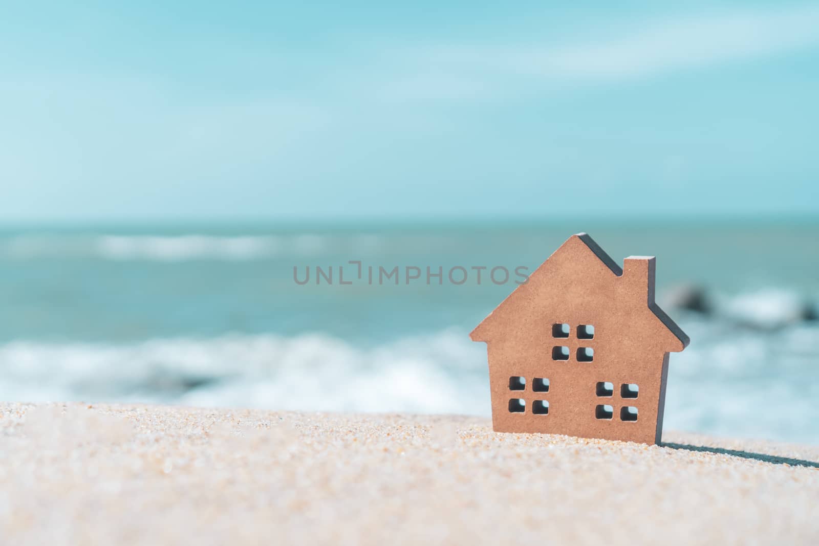 Model of a little house on sand with nature beach background. Dream life concept.