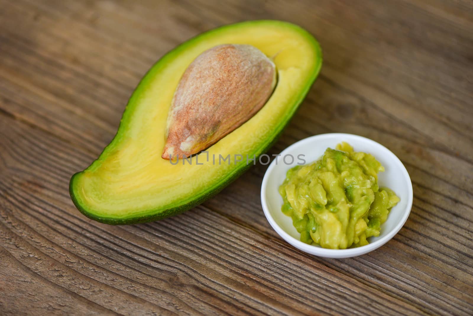 Avocado sliced half and avocado dip mashed on wooden background / Fruits healthy food concept