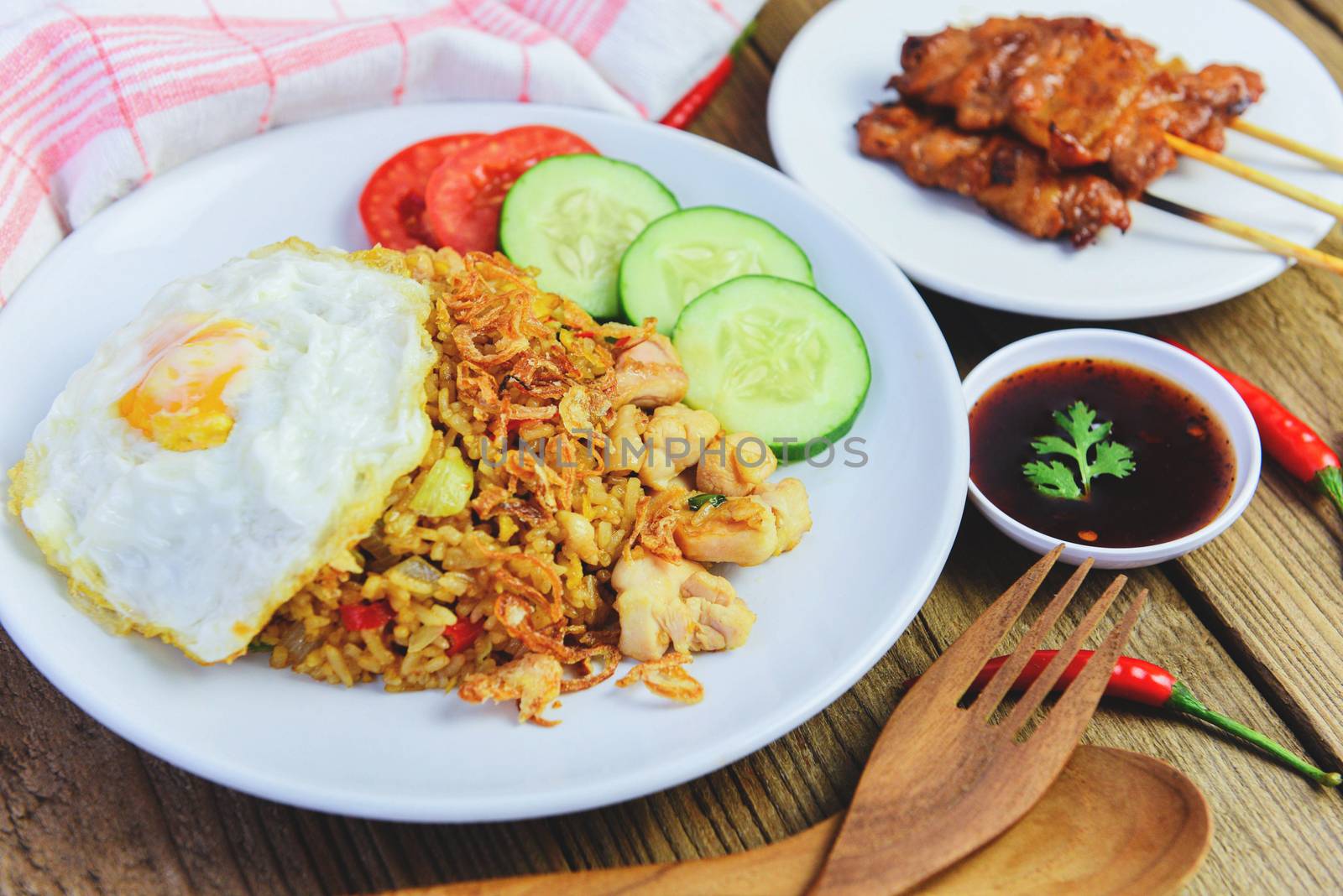 Nasi goreng fried rice chicken with egg tomato cucumber on white plate and satay with sauce / Nasi Goreng Ayam indonesian food Asian