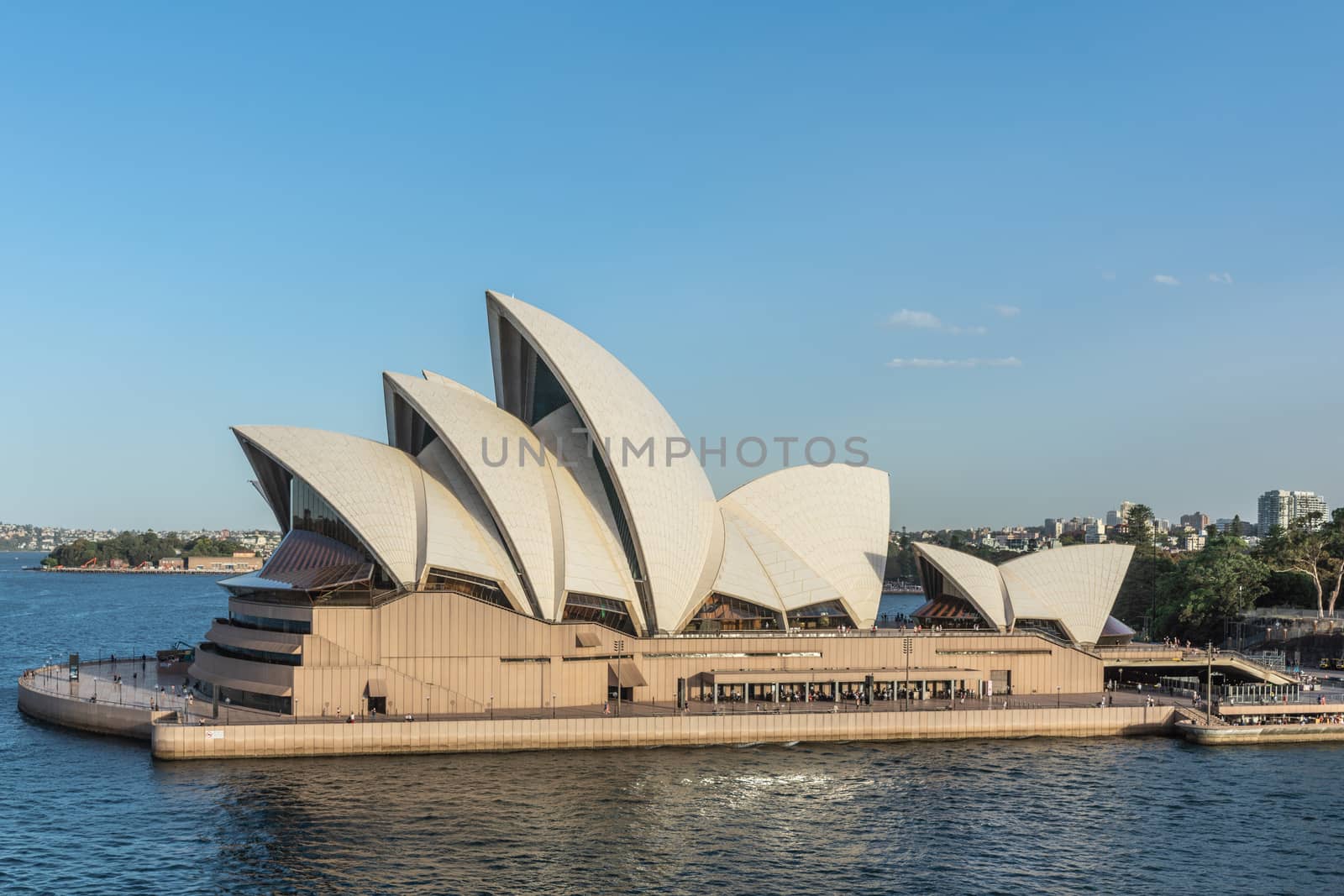 Sydney, Australia - February 12, 2019: Closeup of Side view of the Opera House during sunset. Blue sky and water. Horizon is shore of bay.