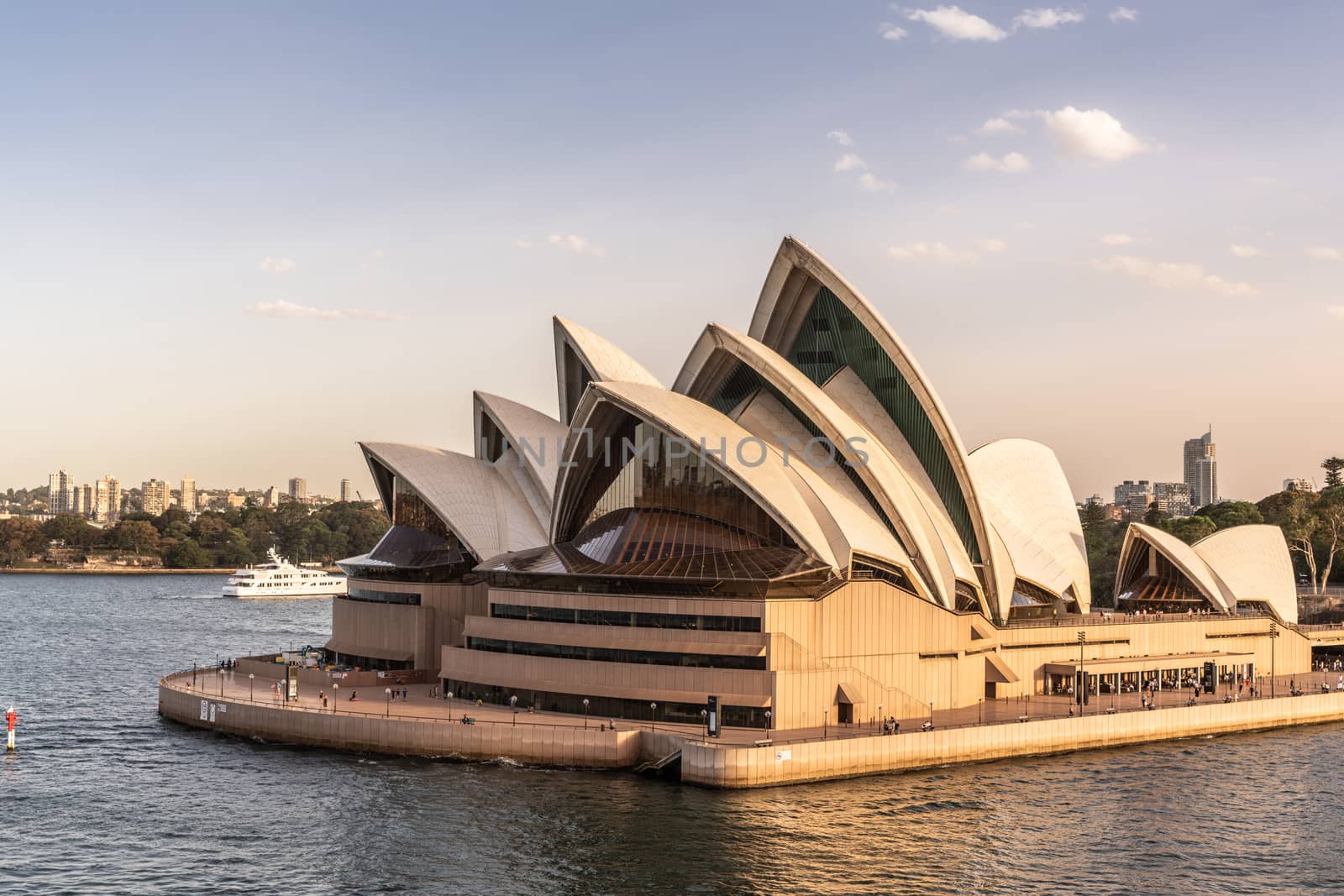 Sydney, Australia - February 12, 2019: Northwest corner view of the Opera House with ferries in front. Blue sky and water. Horizon is north shore of bay.