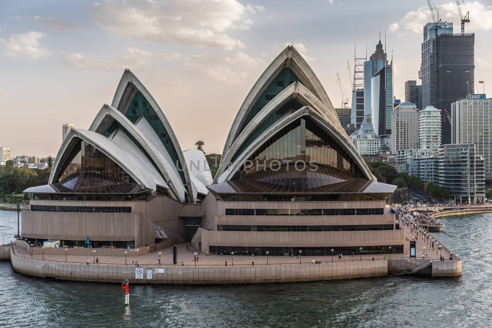 Sydney, Australia - February 12, 2019: Closeup of North side of the Opera House with highrises. Light Blue sky and gray water.