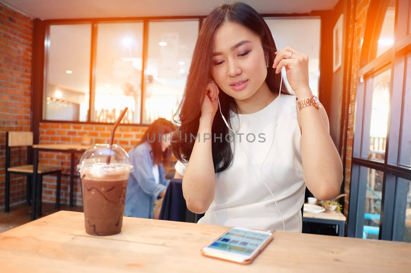 Young woman listening to music in coffee shop by Surasak